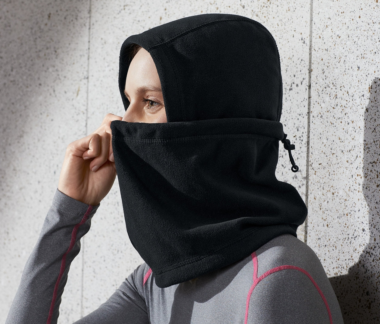 Femme ajustant une cagoule noire en micropolaire sur sa tête.