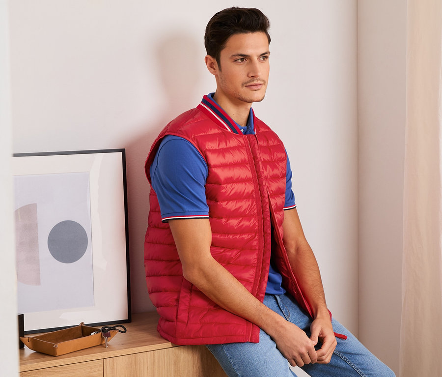 Un homme est assis et porte un gilet surpiqué rouge.