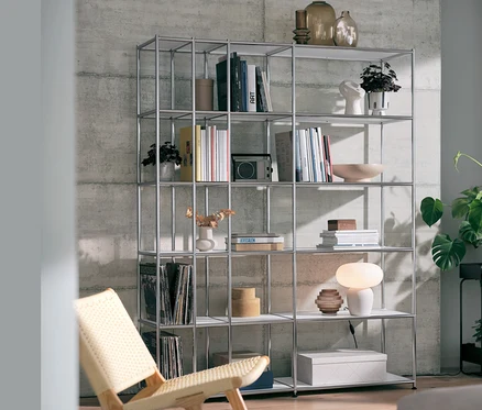 Une étagère ouverte en métal « CN3 » blanche avec une lampe de table avec abat-jour en verre et un fauteuil relax.
