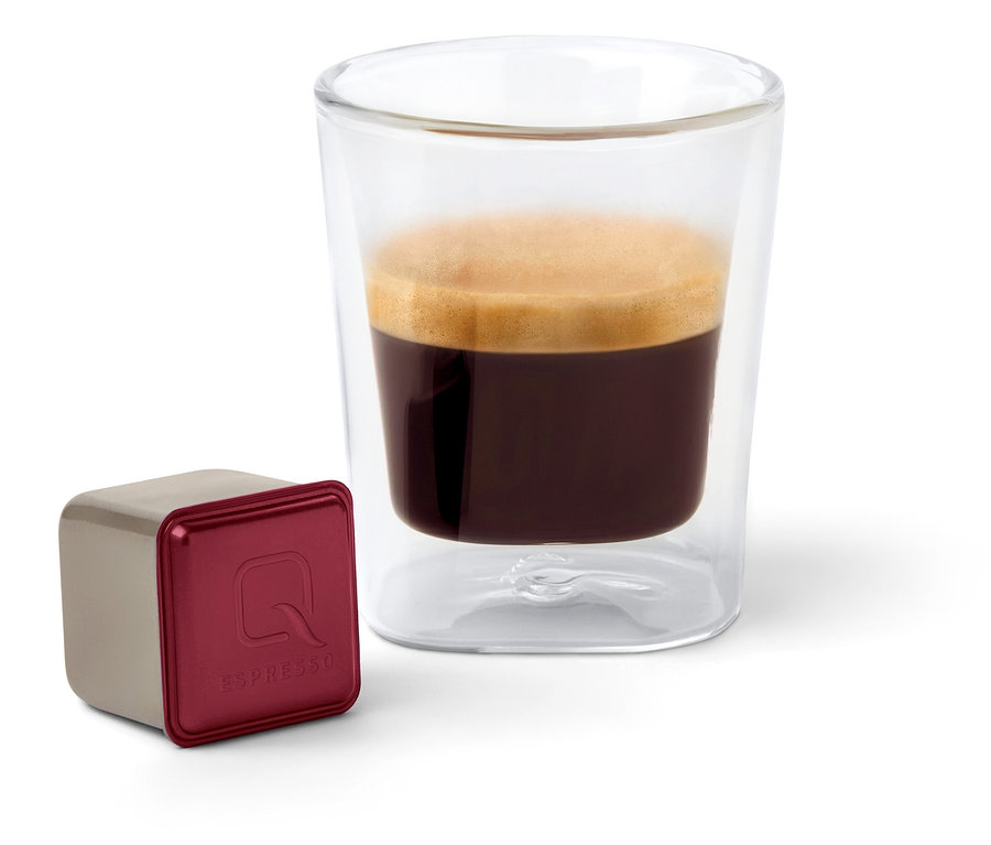 Une capsule Qbo Espresso APANECA ANA est à côté d'un verre à espresso.