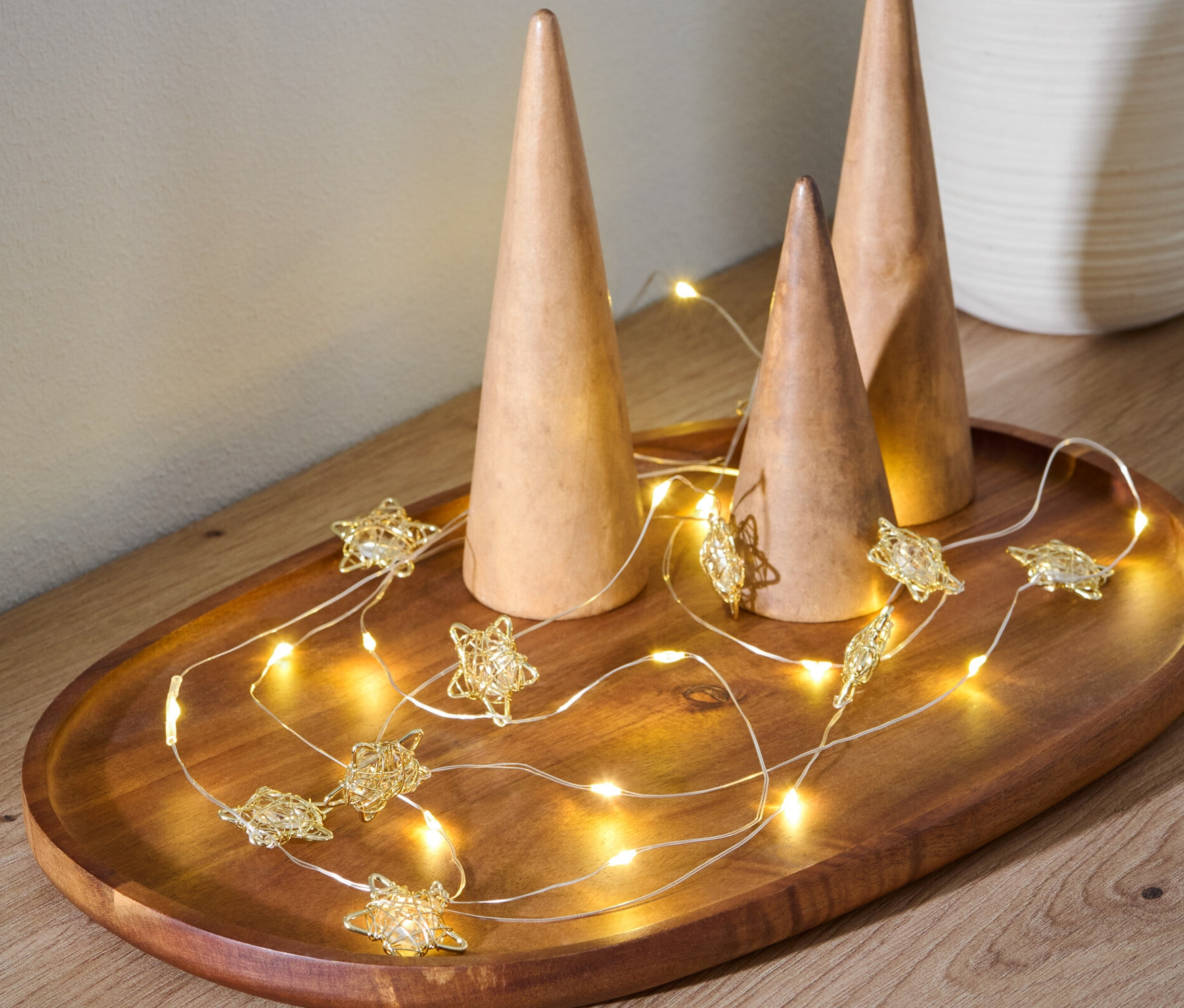 Sur un plateau en bois reposent trois cônes en bois et une guirlande lumineuse à LED en forme d'étoile.