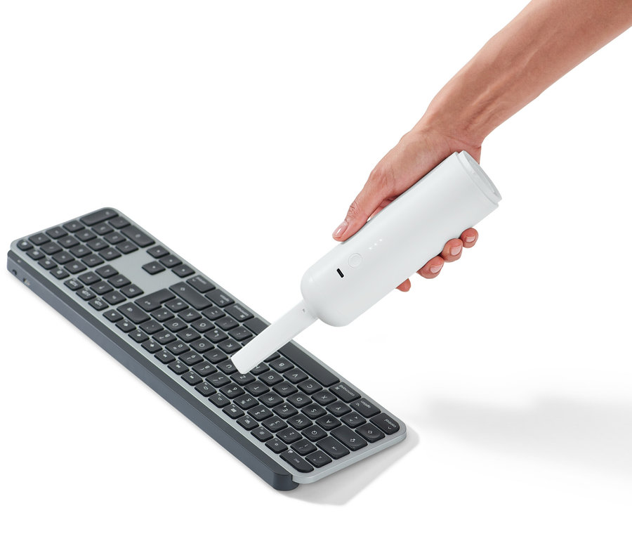 Une main tient un aspirateur à main au-dessus d'un clavier.