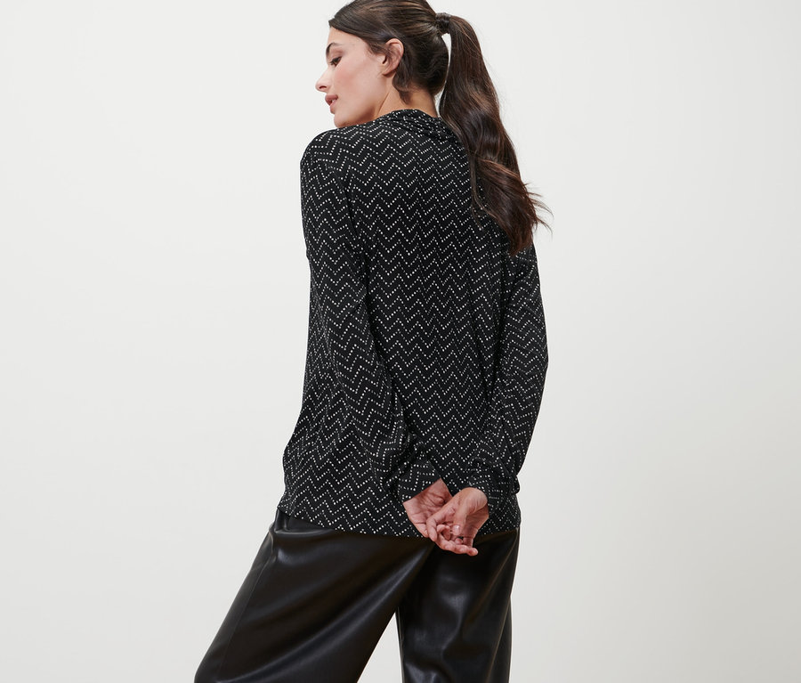 Une femme pose, dos à la caméra, portant un t-shirt manches longues avec encolure en V, imprimé intégral et un pantalon en similicuir noir.