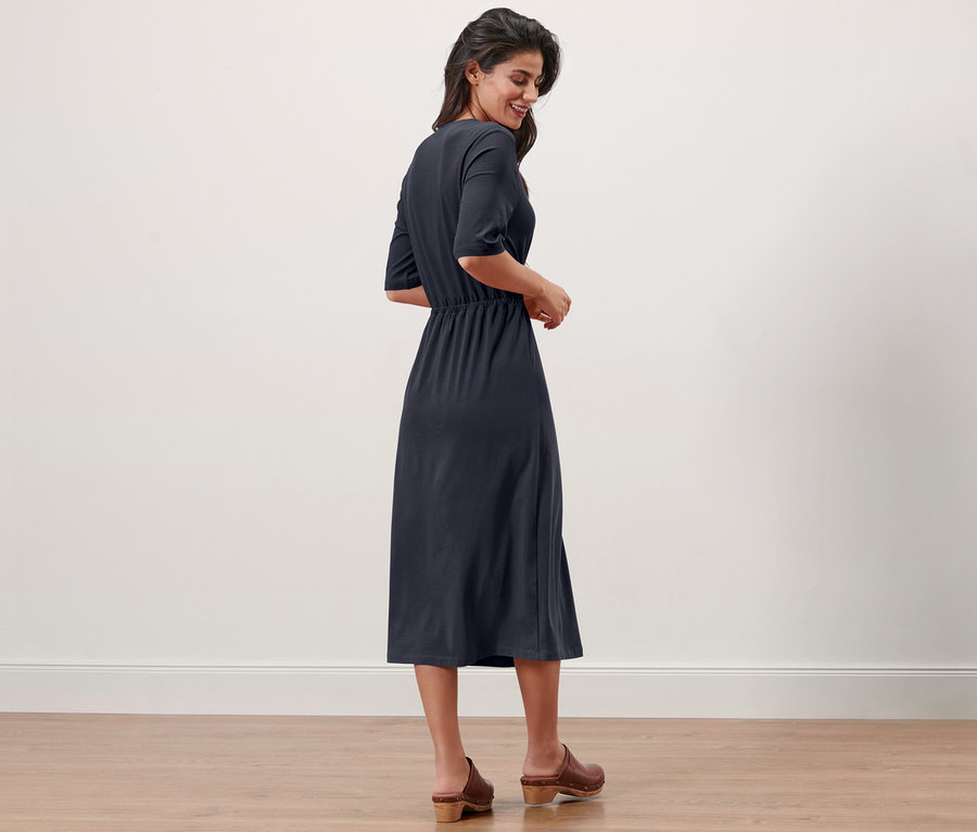 Une femme se tient de côté et sourit, elle porte une robe en jersey bleu marine.