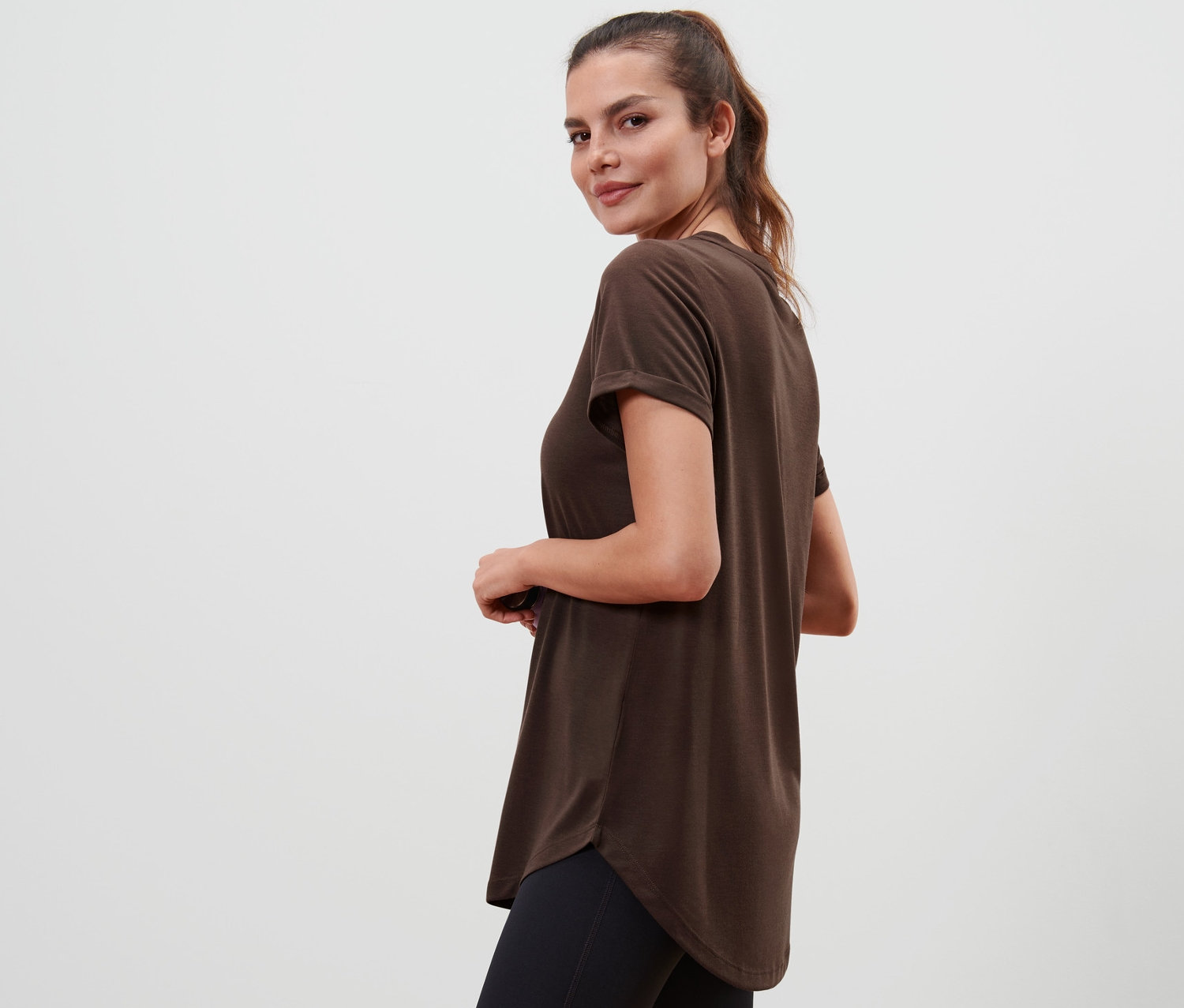 Une femme regarde par-dessus son épaule et porte un t-shirt long marron.