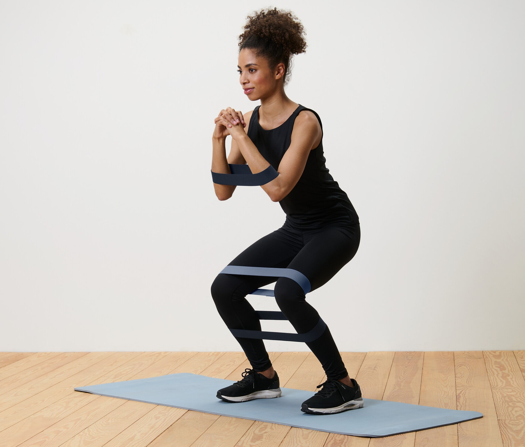 Femme faisant des squats avec 3 bandes d'entraînement sur un tapis.