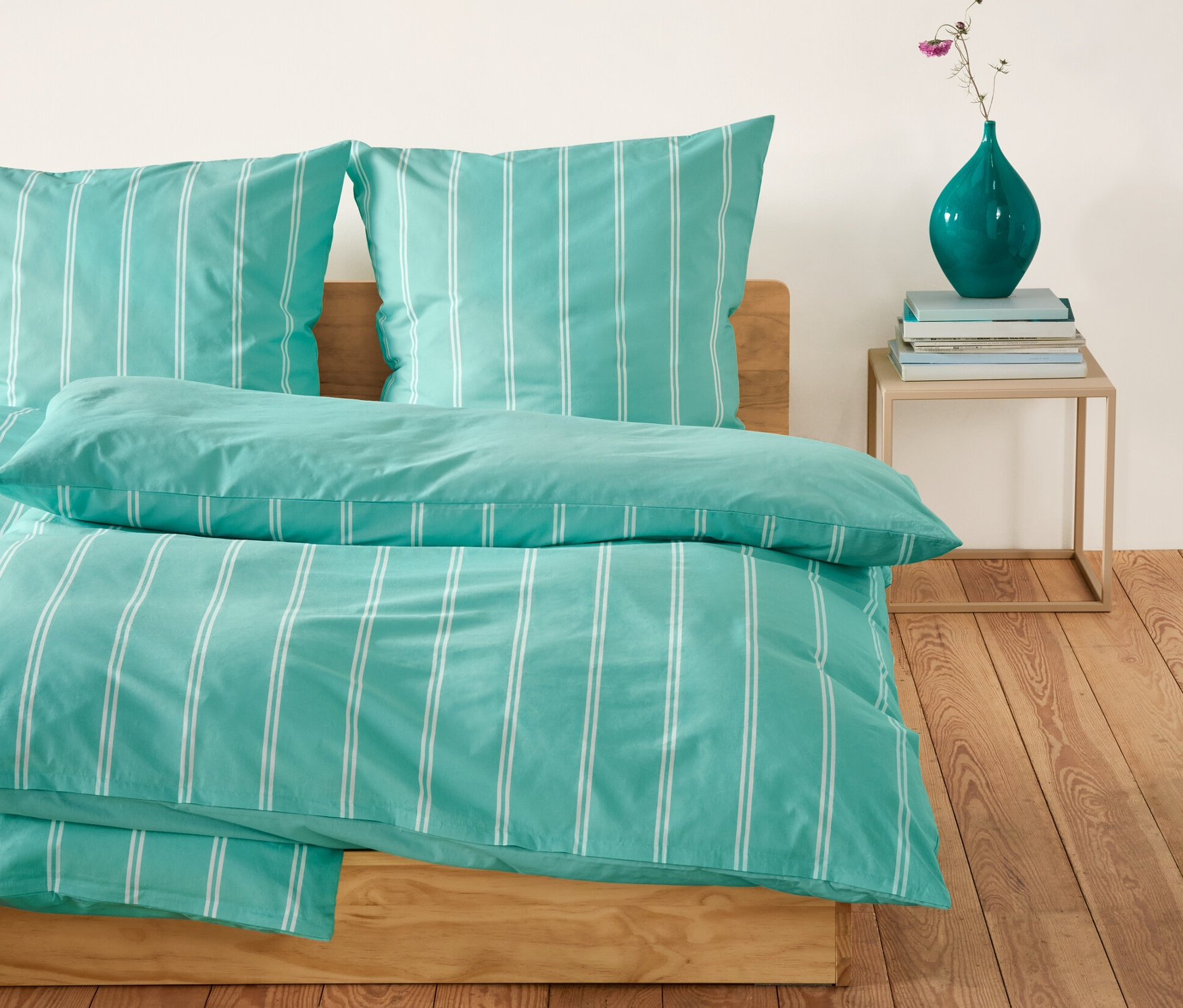 Parure de lit en renforcé à rayures bleu et blanc sur un lit. Une table avec un vase est à côté du lit.