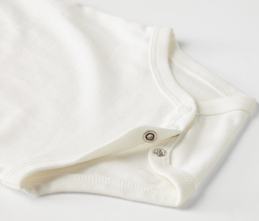 Gros plan sur un body blanc pour bébé à manches courtes avec boutons-pression.