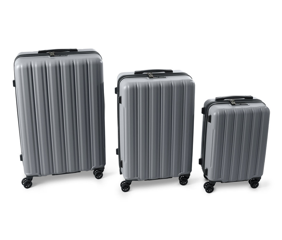 Trois valises rigides grises (grande, moyenne et petite) sont placées côte à côte sur un fond blanc.