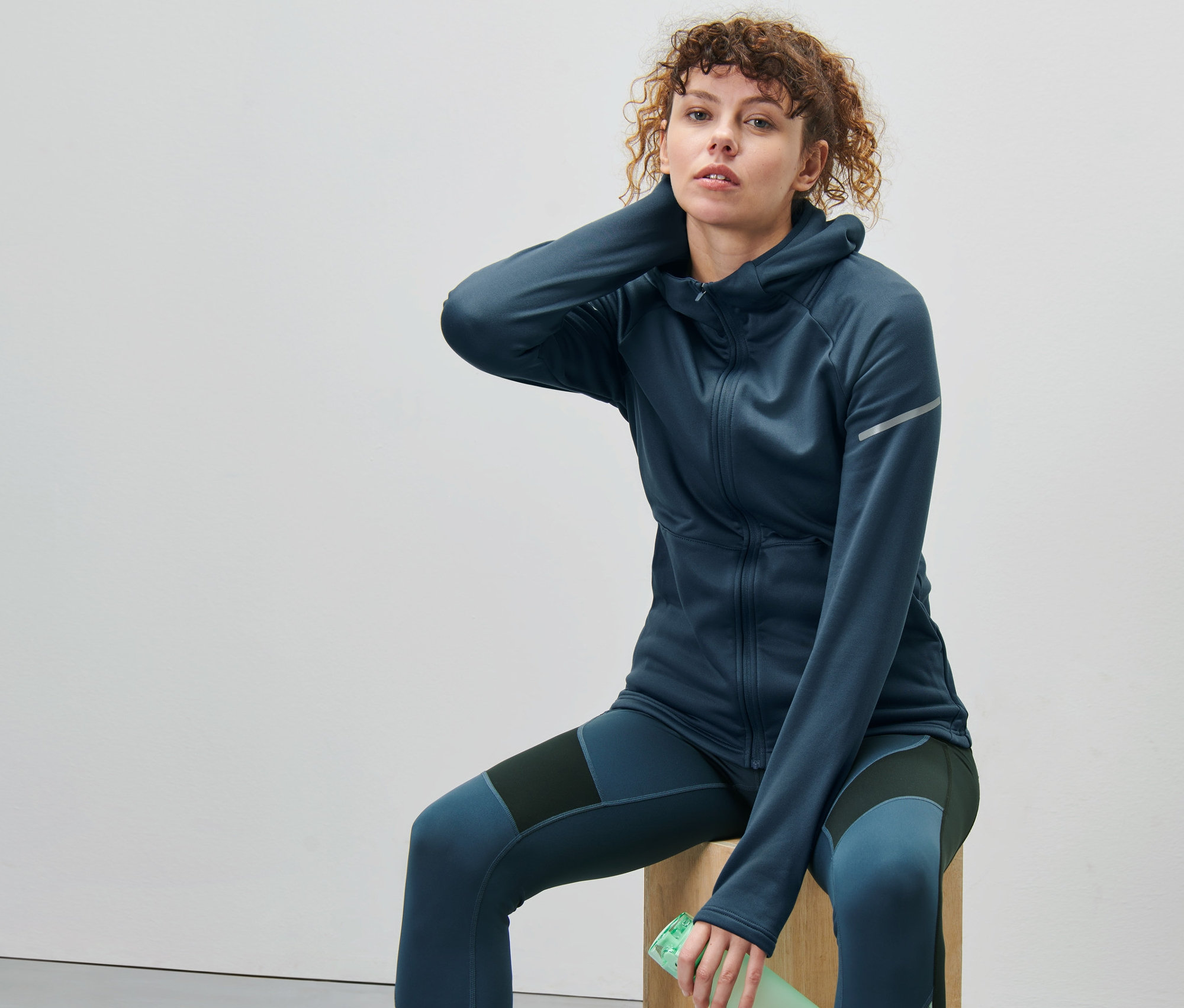 Femme assise sur un cube en bois portant une veste thermique bleu foncé.