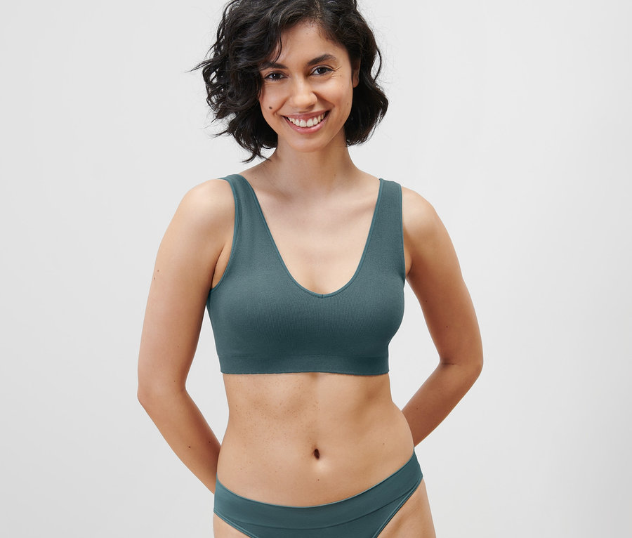 Une femme souriante porte un bustier sans coutures pétrole et un bas de bikini.