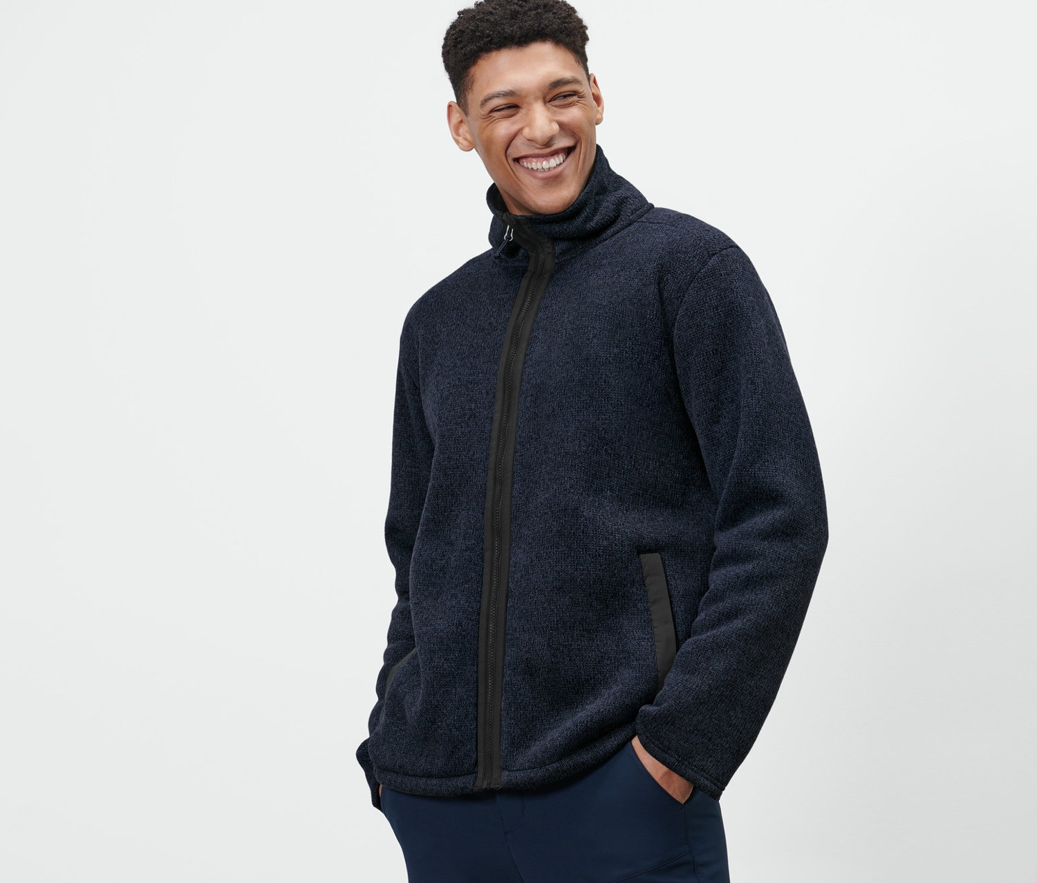 Un homme pose, les mains dans les poches, portant une veste en maille polaire.