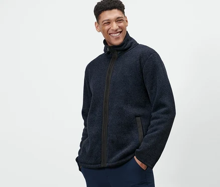 Un homme pose, les mains dans les poches, portant une veste en maille polaire.