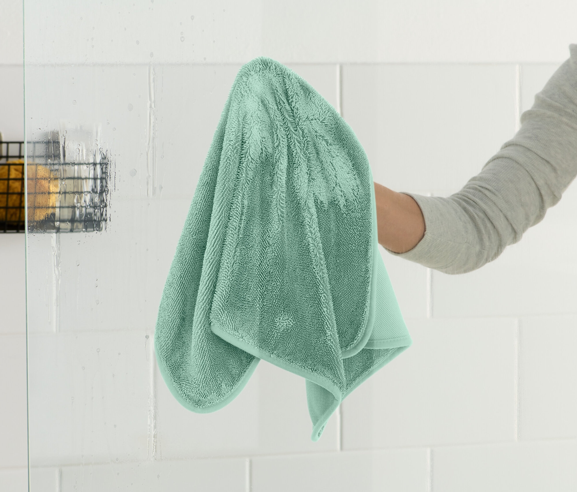 Une main essuie une paroi de douche en verre avec un chiffon sec très absorbant.