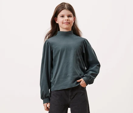 Une fille pose en T-shirt manches longues pour enfants, bleu ardoise, et en jean noir.