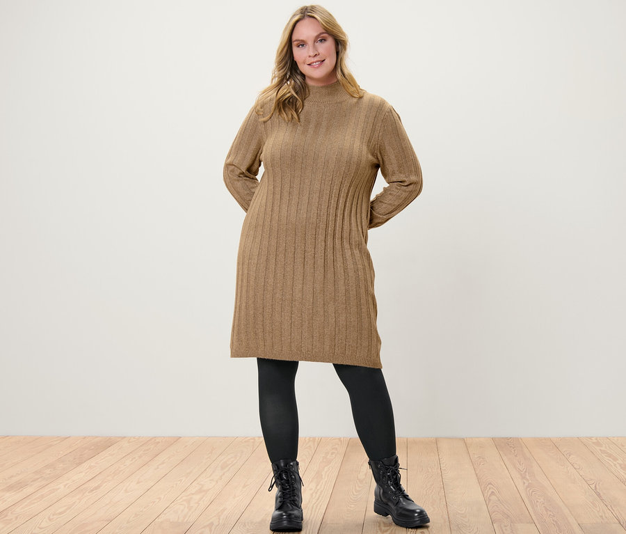 Femme posant en robe en maille côtelée avec col montant, collants fins noirs 80 DEN et bottes noires.