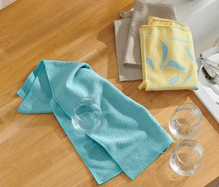 Trois linges de cuisine et trois verres sont posés sur un plan de travail.