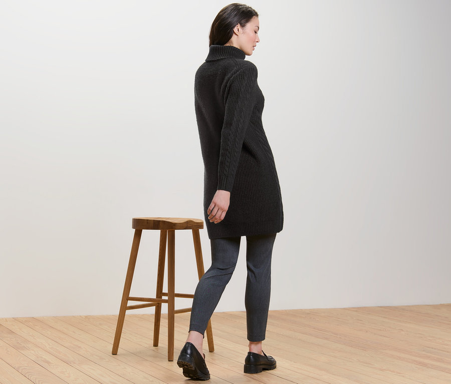 Femme vue de dos portant un long pull en maille noire avec torsades.