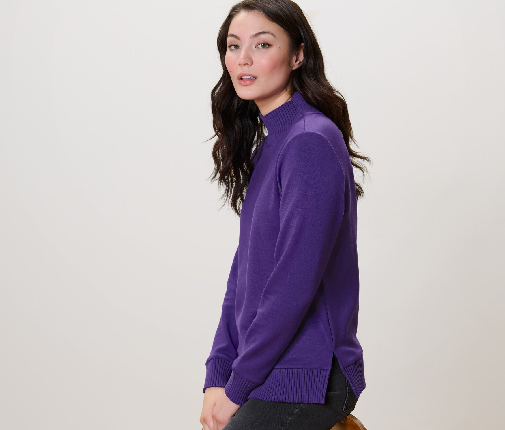 Une femme est assise de côté et porte un sweatshirt violet à col montant.