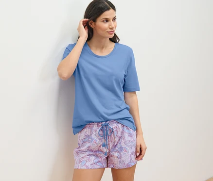 Femme en ensemble pyjama shorty appuyée contre un mur.