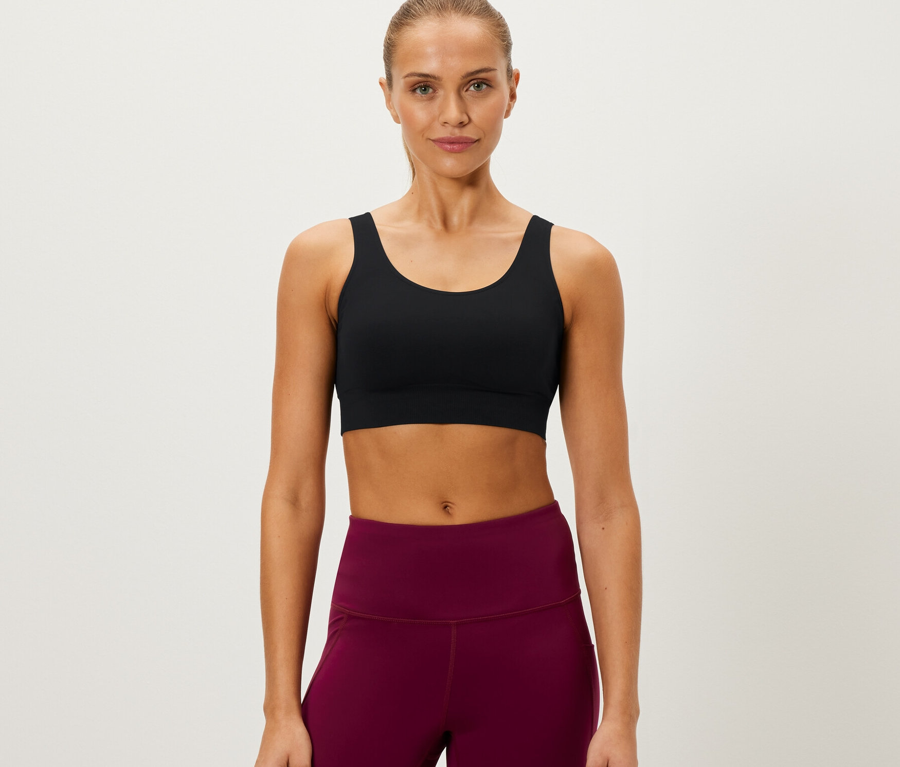 Une femme porte une brassière de sport Seamless, noir, et un legging bordeaux.