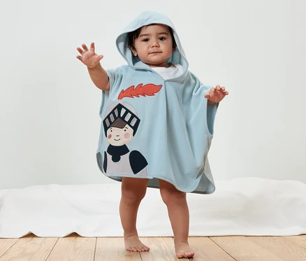 Un enfant pose dans un poncho bleu clair en éponge, chevalier avec capuche.