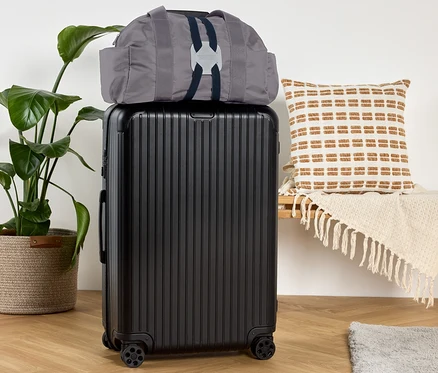 Un sac gris est posé sur une valise noire, à côté d'un banc avec un coussin.