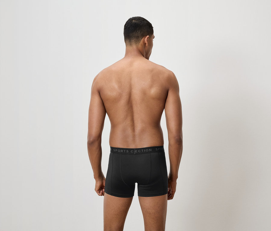 Un homme, dos à la caméra, porte un caleçon boxer noir.