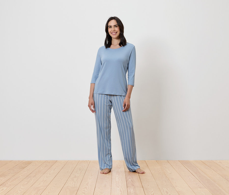 Une femme debout portant un pyjama bleu rayé.