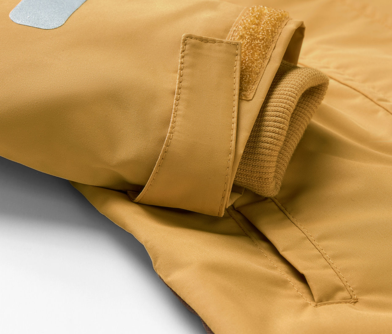 Détail d'une combinaison de pluie pour enfant avec poche et élément réfléchissant.