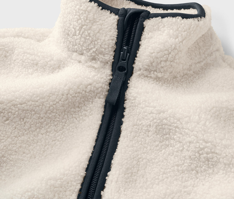 Détail d'une veste en peluche teddy pour enfant avec fermeture éclair et bordure bleu foncé.