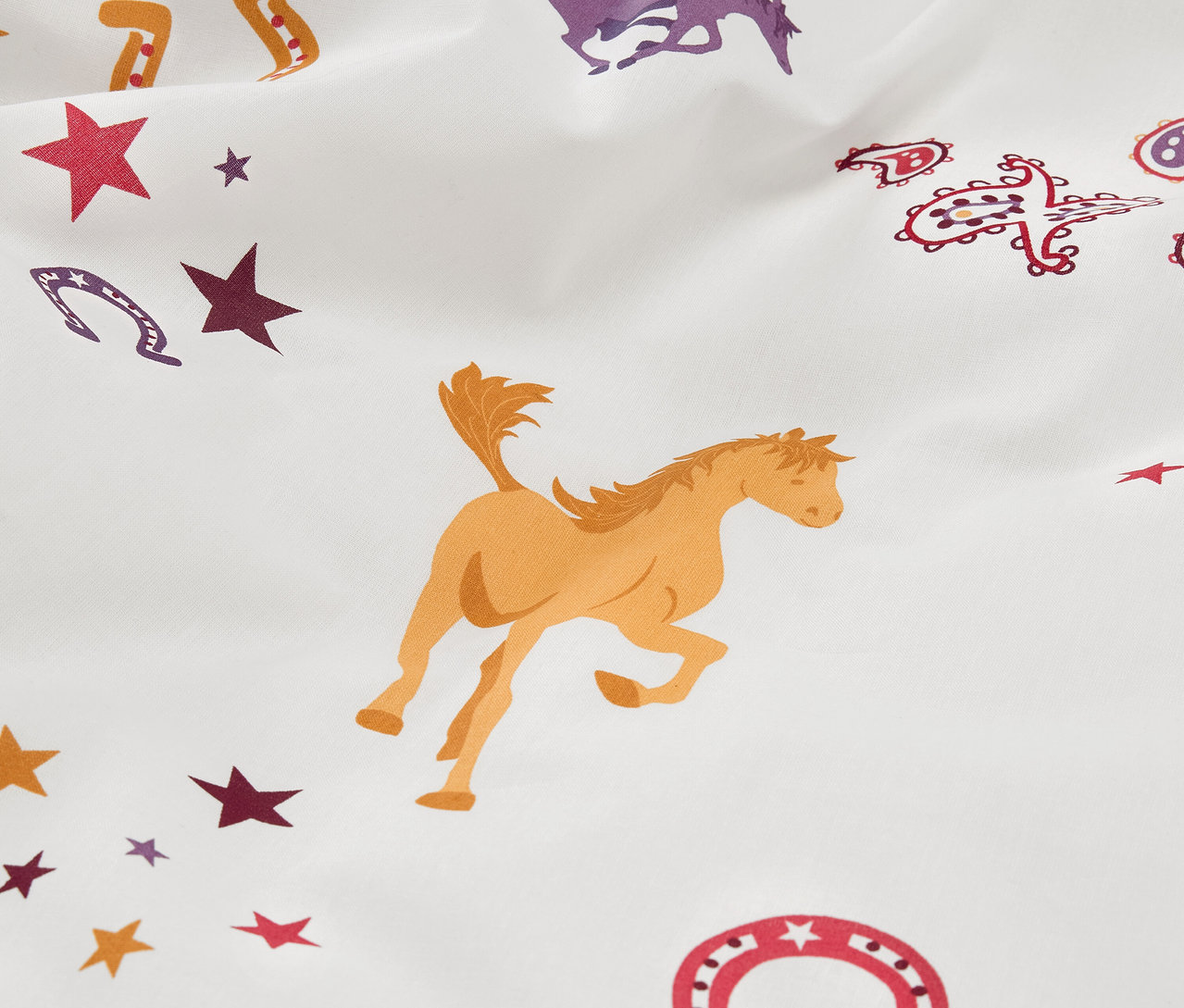 Gros plan sur une parure de lit en renforcé pour enfant avec des motifs de chevaux et d'étoiles.