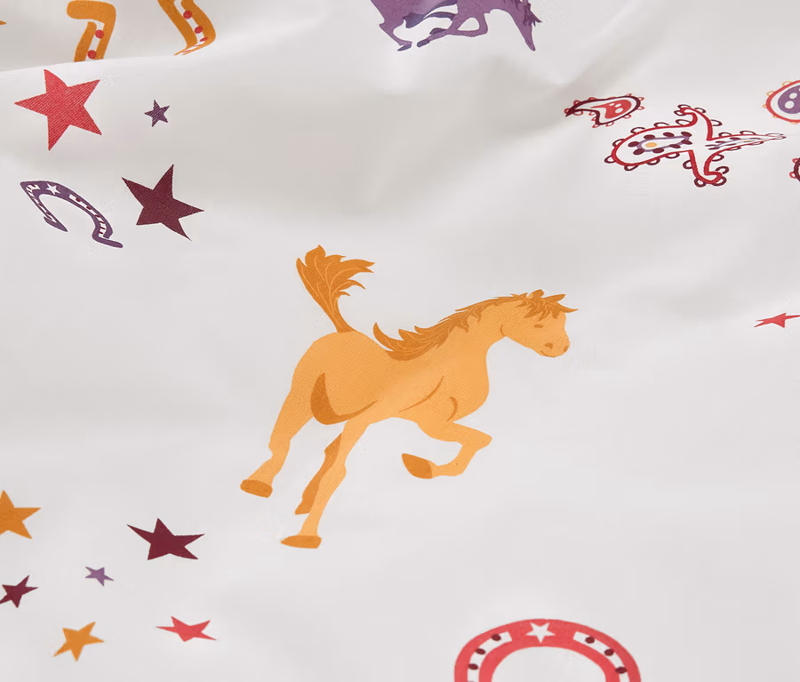 Gros plan sur une parure de lit en renforcé pour enfant avec des motifs de chevaux et d'étoiles.