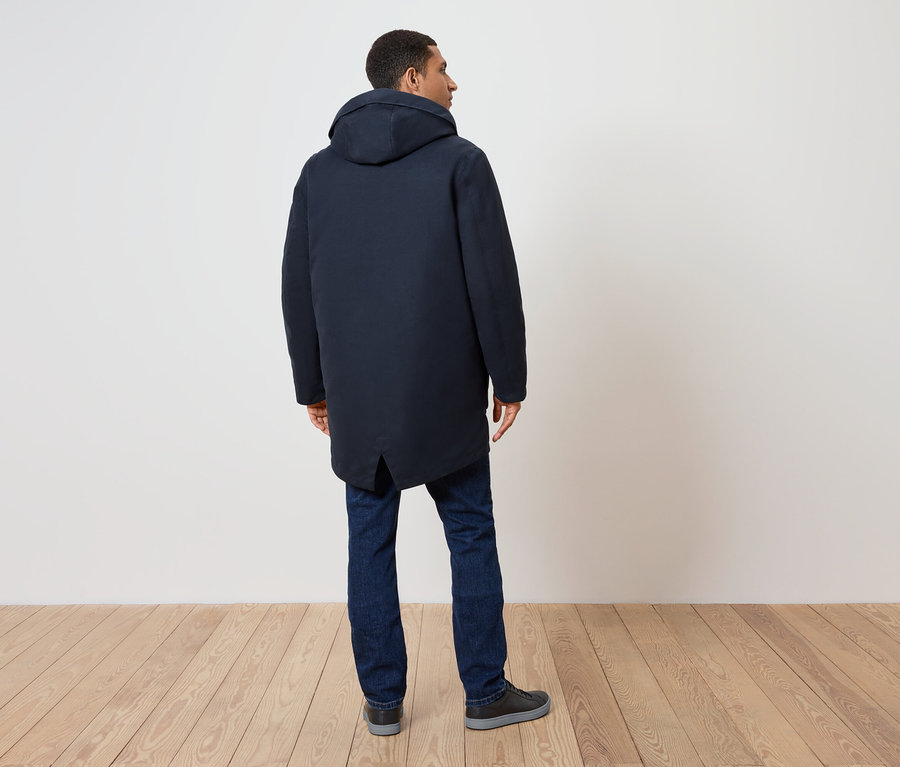 Homme de dos, portant un manteau bleu marine à capuche, un jean et des chaussures.