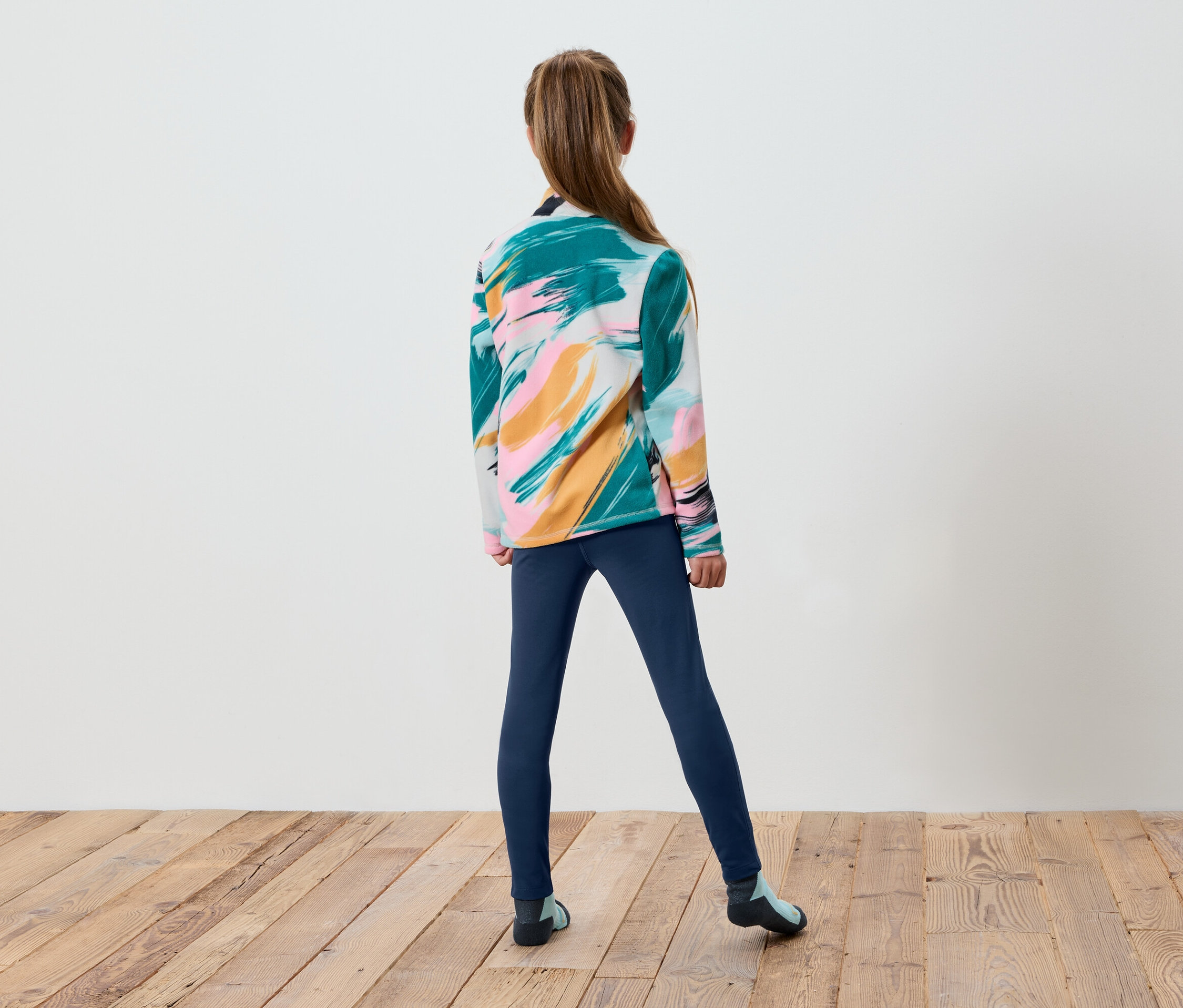 Une fille se tient dos à la caméra, portant un pull coloré et des leggings bleus.