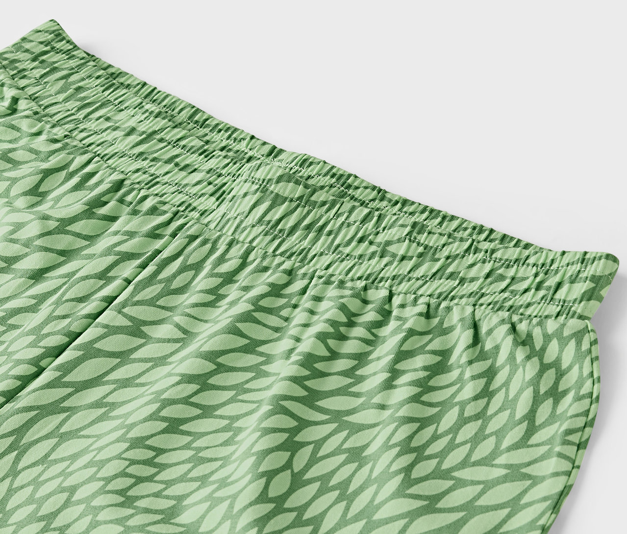 Détail d'un pantalon vert avec taille élastique et motif de feuilles.