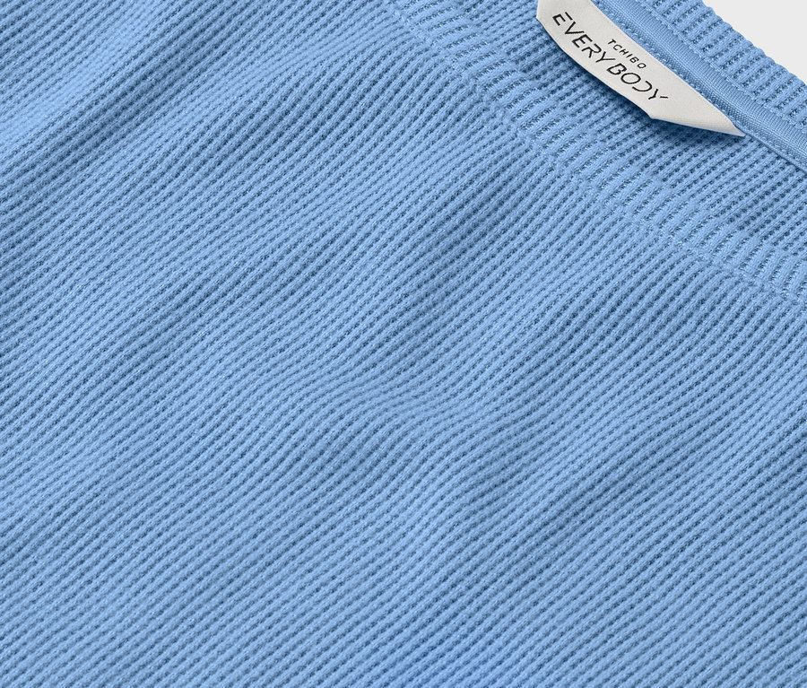 Gros plan d'un tissu bleu clair avec une texture côtelée et une étiquette blanche portant l'inscription EVERYBODY.