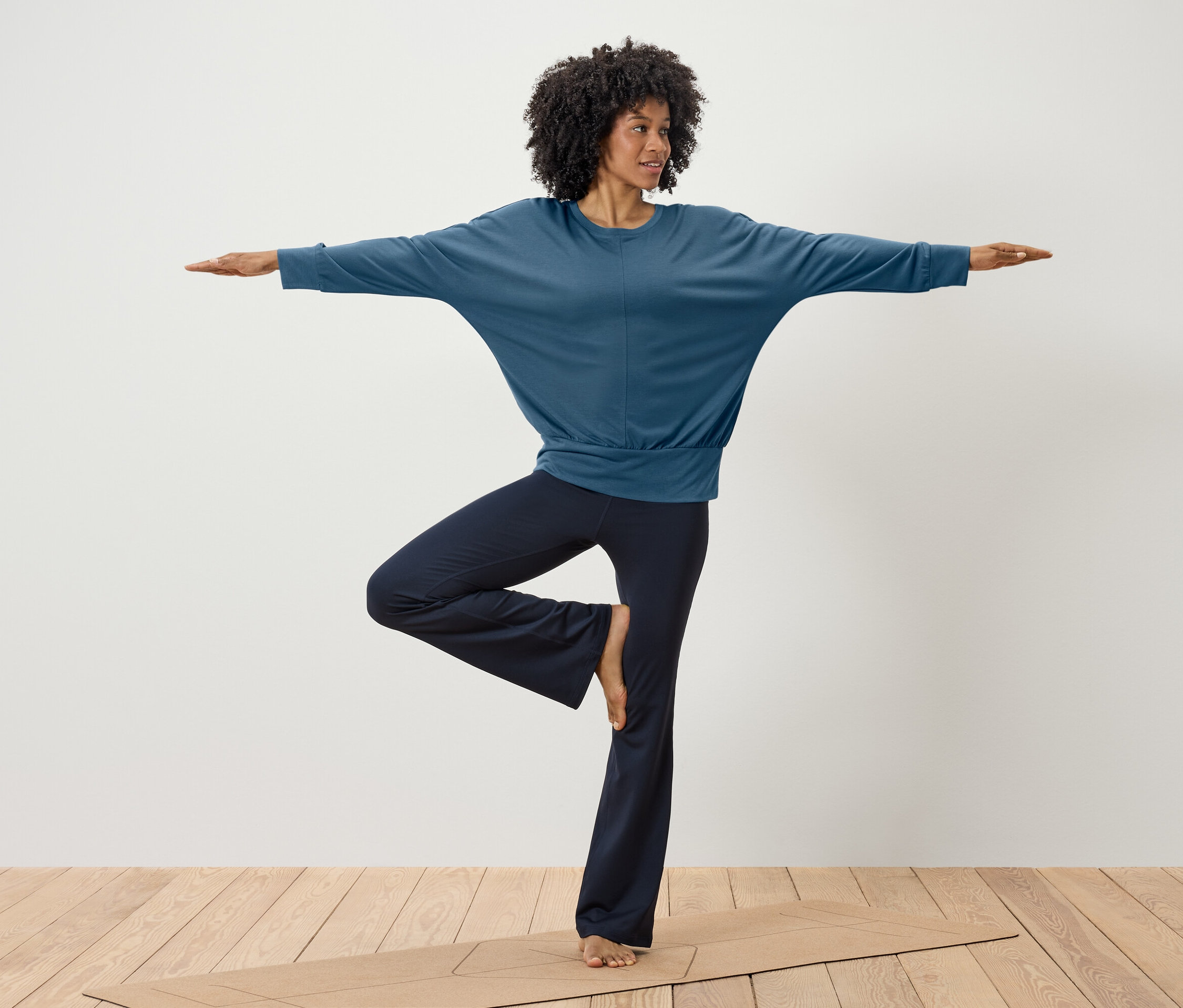 Une femme fait du yoga dans un haut bleu et un pantalon bleu foncé sur un tapis.