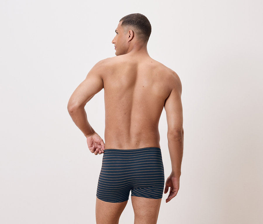 Un homme torse nu pose de dos en portant un boxer rayé.
