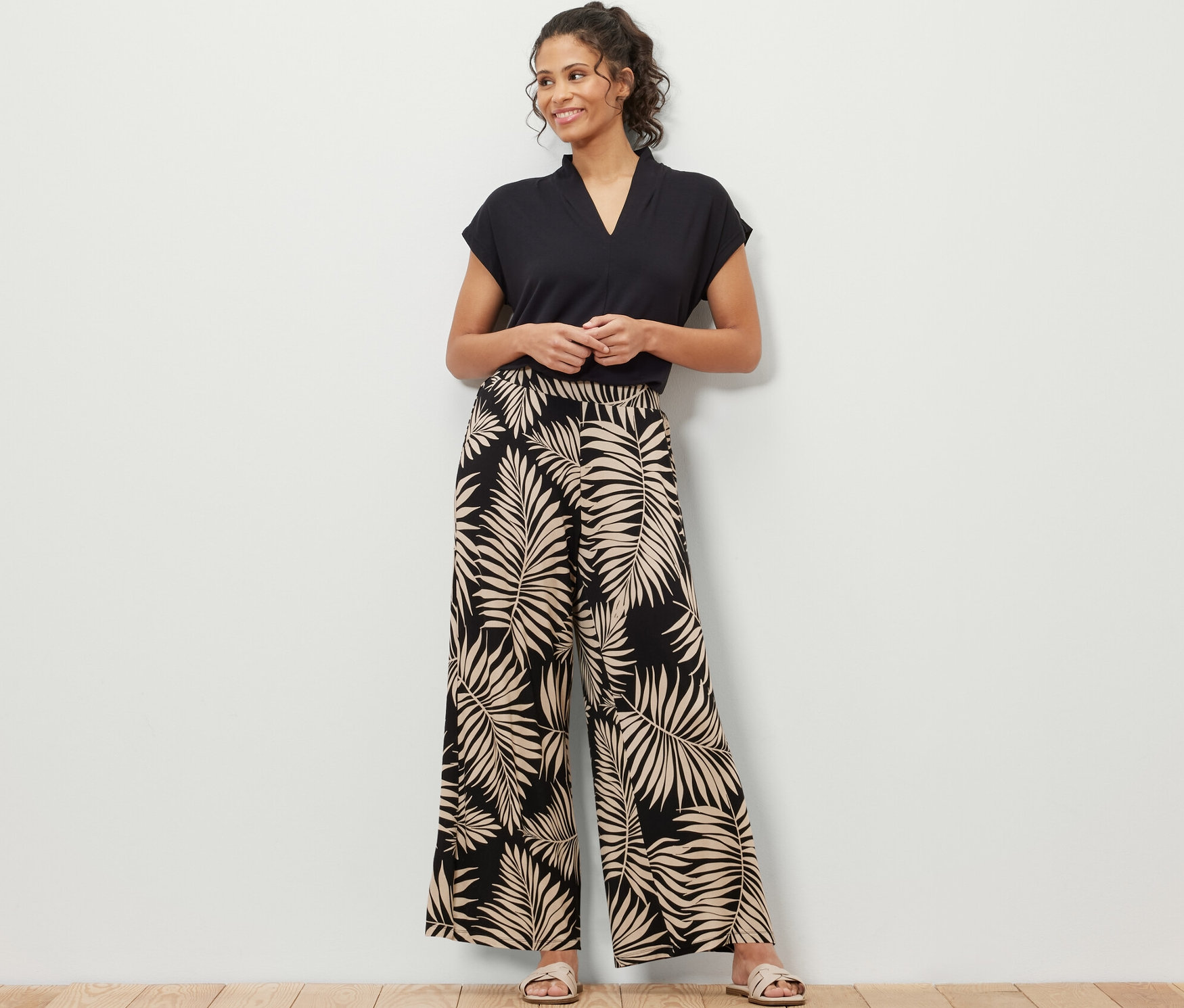 Une femme debout portant un t-shirt noir et un pantalon palazzo imprimé avec un motif de feuilles.