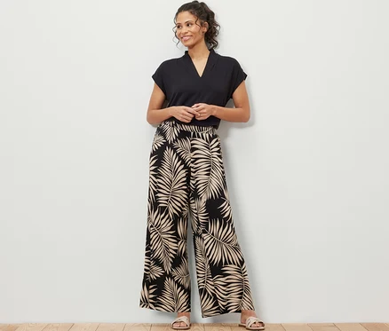 Une femme debout portant un t-shirt noir et un pantalon palazzo imprimé avec un motif de feuilles.