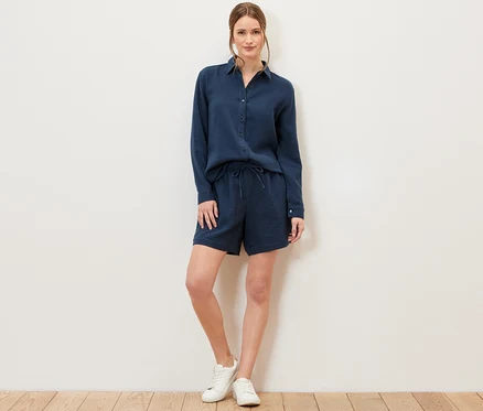 Une femme debout portant un chemisier en mousseline bleu marine et un short.