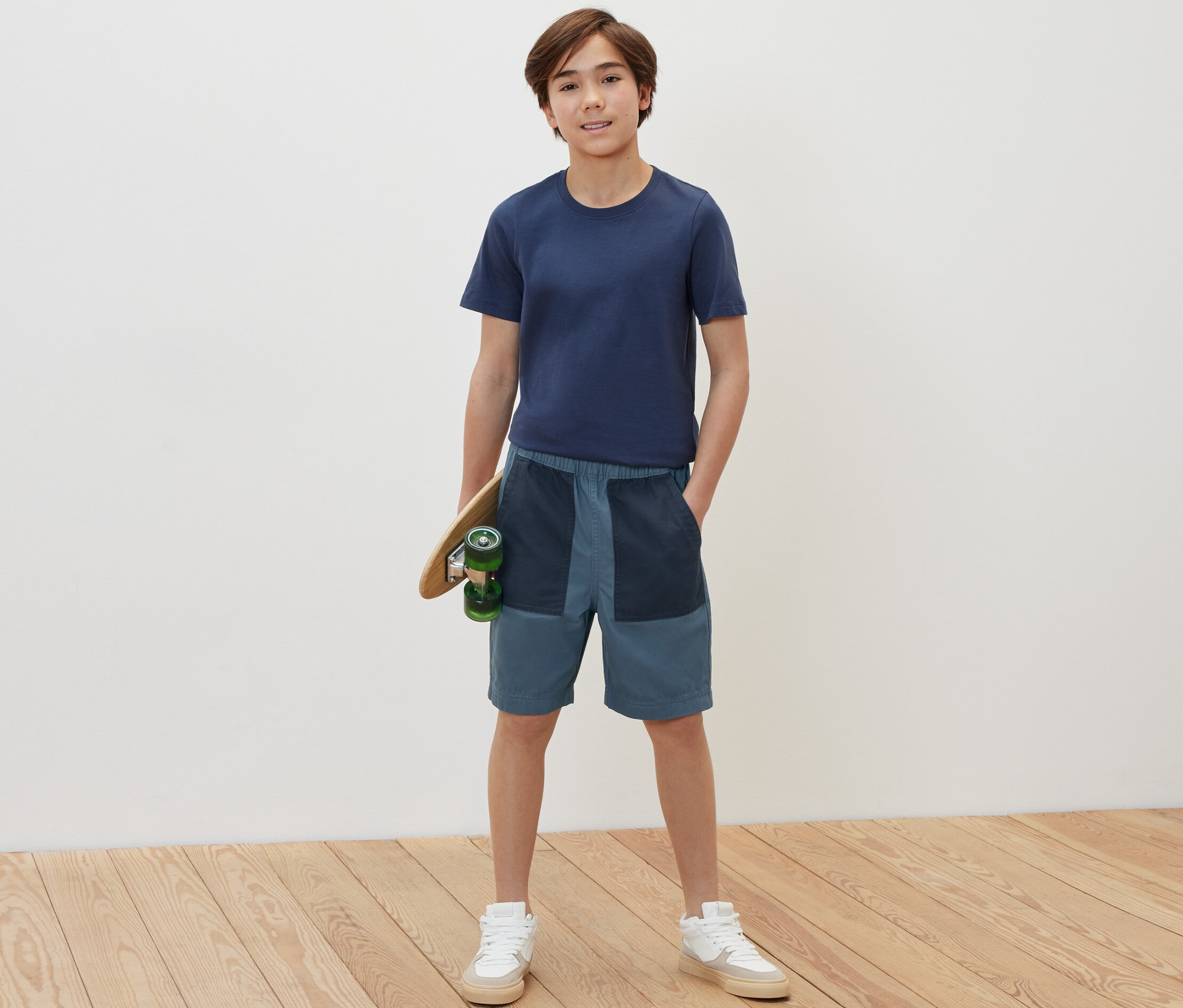 Un garçon tient un skateboard et porte un bermuda pour enfant.