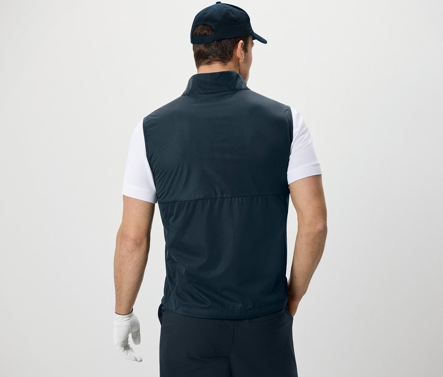Homme vu de dos portant une veste en softshell, un t-shirt et une casquette.