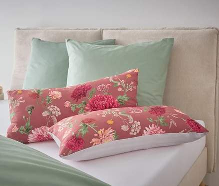 Sur un lit, deux oreillers verts et deux oreillers oblongs à motifs floraux.