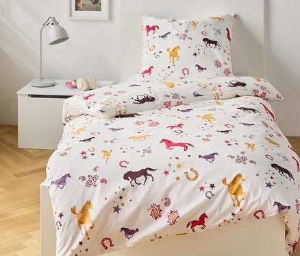 Lit avec des draps blancs imprimés avec des chevaux, des fers à cheval et des étoiles.