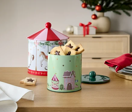 Deux boîtes à biscuits décorées en métal sur une table en bois avec des décorations de Noël en arrière-plan.