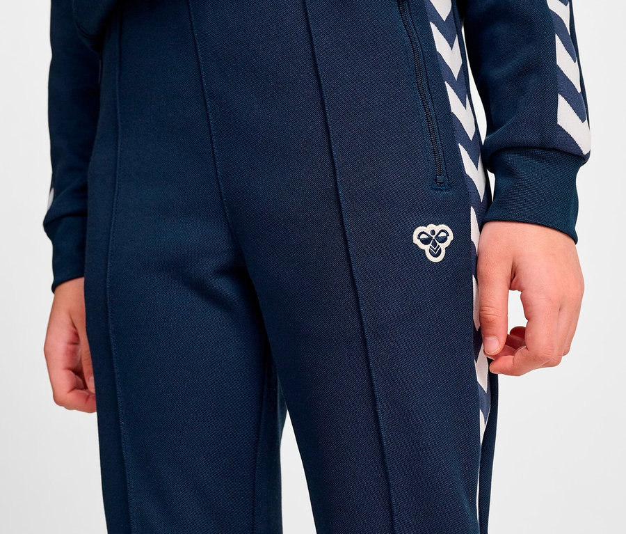 Une personne porte un pantalon de survêtement bleu marine avec des flèches blanches sur le côté.