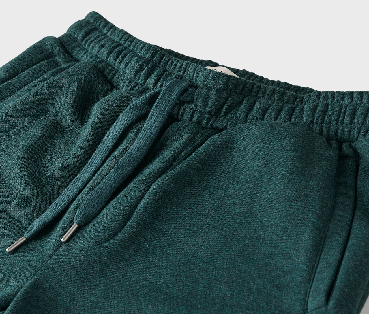 Détail d'un pantalon de survêtement vert avec taille élastique et cordon de serrage.