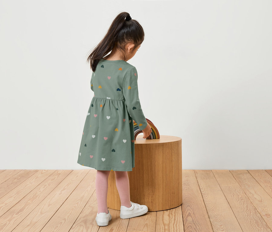 Une fille en robe verte avec des coeurs se tient près d'une table en bois avec un arc-en-ciel.